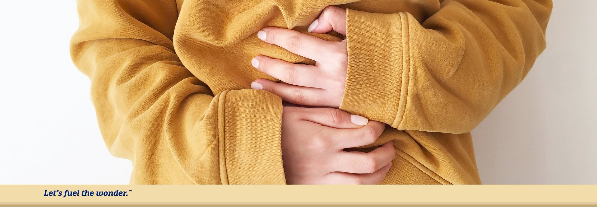 Person wearing a yellow sweater gripping left and right hands on belly to help suppress stomach cramps