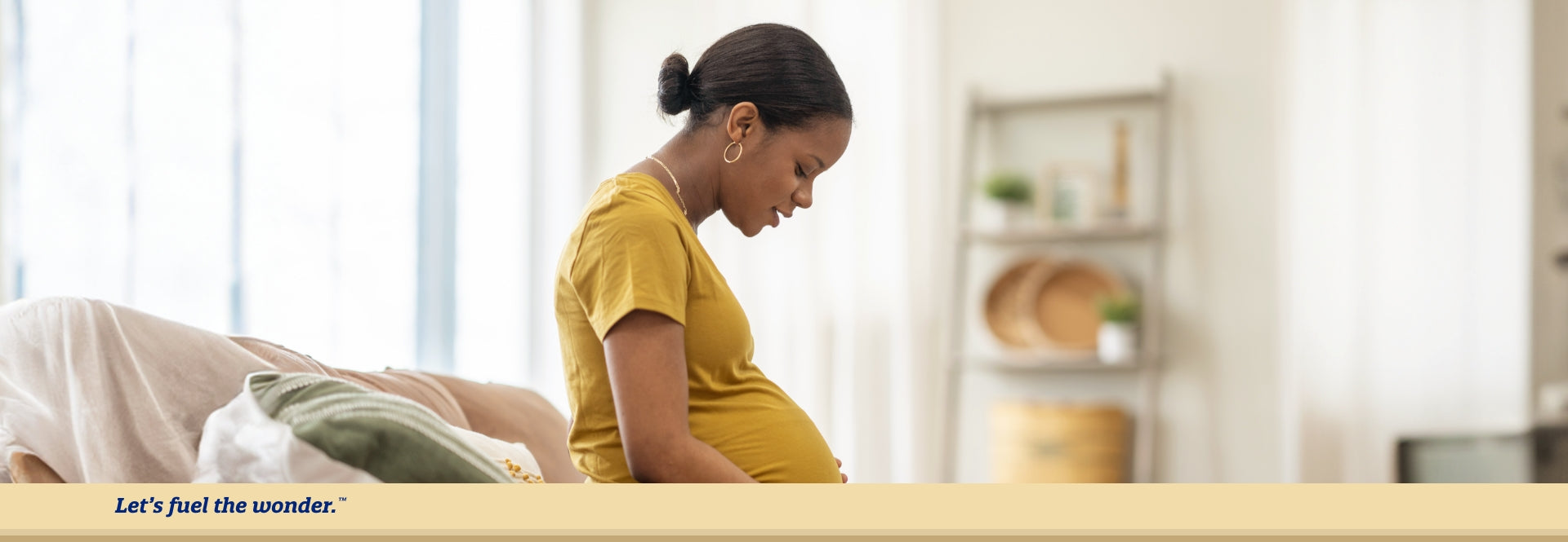 Pregnant parent looking down at pregnant belly while sitting on couch upright