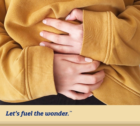 Person wearing a yellow sweater gripping left and right hands on belly to help suppress stomach cramps